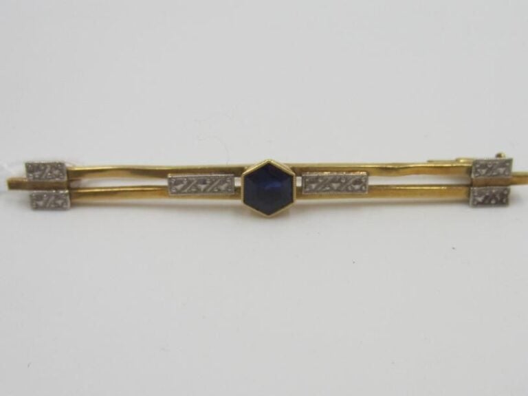 BROCHE BARRETTE en or jaune et or gris (750 millièmes) ajouré à motifs géométriques centré d'une pierre bleue hexagonal