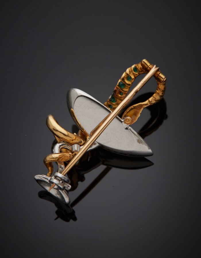BROCHE "caducée" en or jaune et or gris (750‰) ajouré, serti d'émeraudes et dia…