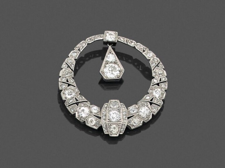 • BROCHE circulaire en platine (950‰) et or gris (750‰) ajouré, serti de diamants taille ancienne et taillés en rose, retenant en pampille une goutte stylisée pavée d'un diamant rond et d'un diamant taille ancienne de forme coussin plus importan