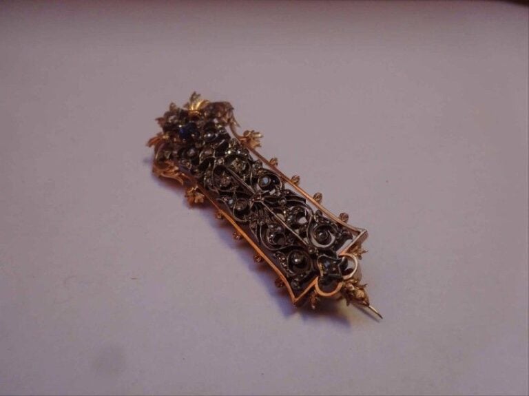 BROCHE en or rose 18K (750°/00) et argent (925°/00) ciselé à motif de feuillages et d'enroulements serti de diamants taille rose et d'un saphir taille coussi