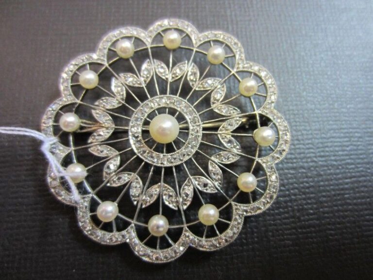 BROCHE «fleur» stylisée en or gris (750 millièmes) ajouré serti de perles de culture de couleur blanche, dont une au centre plus importante, entouré de diamants taillés en ros