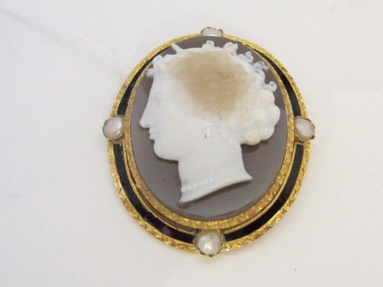 BROCHE ovale en or jaune (750 millièmes) ajouré et ciselé, serti d’un camée en onyx trois couches « profil de femme » souligné d’émail noir (restauration) et ponctué de quatre demi perles baroque