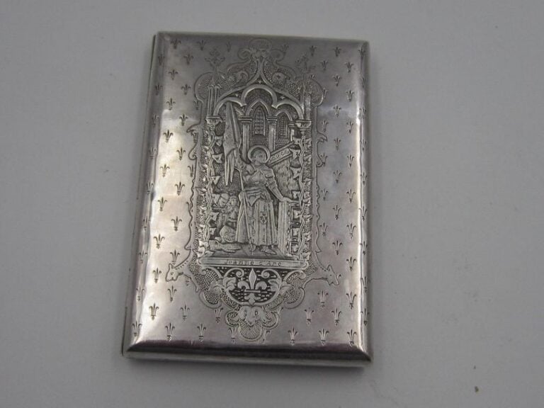Carnet en argent (minimum 800 millièmes), à décor de l'effigie de Jeanne d'Arc dans un cartouche, sur semis de fleurs de lys ; grande fleur de lys gravée au rever