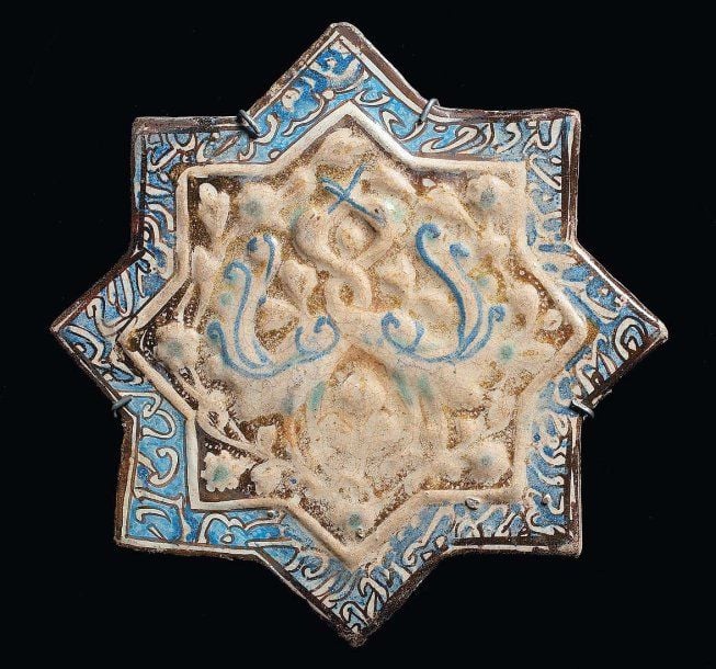 CARREAU AUX ÉCHASSIERS Étoile de revêtement octogonale, décorée en relief et lustre métallique d'un couple d'échassiers aux cous entrelacés et d'une frise d'inscriptions cursives en réserve blanche sur fond ble