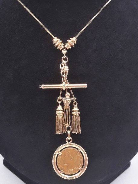 CHAINE GILETIERE en or jaune (750 millièmes) retenant un bâtonnet clef de montre, deux pompons et une pièce de 20 Francs français, en or (900 millièmes) datée 180