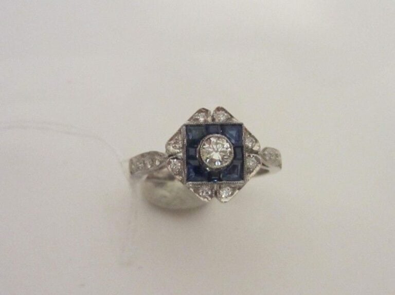 Charmante BAGUE en or gris (750 millièmes) serti de diamants taille brillant, dont un au centre plus important, et saphirs calibrés, à motifs géométrique