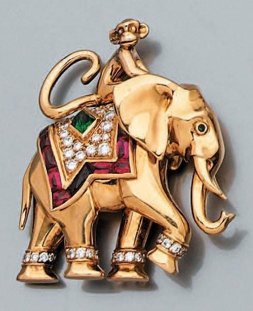 CLIP DE CORSAGE «éléphant chevauché par un petit singe», en or jaune serti d'une émeraude taillée en pain de sucre, d'un pavage de diamants, d'un alignement de rubis calibrés et suifés et de deux petites émeraude