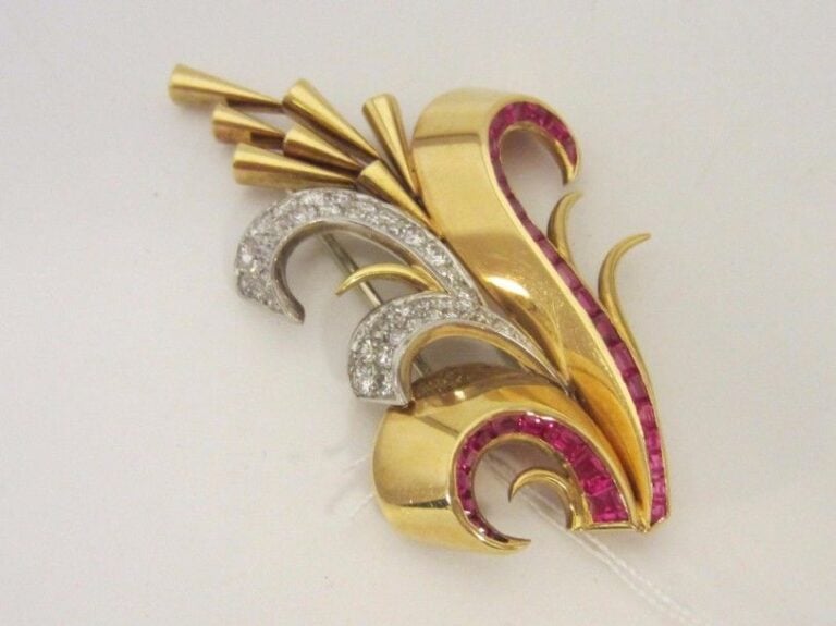 CLIP de CORSAGE « volute stylisée » en or jaune et or gris (750 millièmes) ajouré serti de deux lignes de pierres rouges calibrées et diamants taille brillan