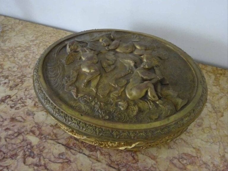 COFFRET A BIJOUX ovale en laiton martelé et repoussé à décor de putti et de guirlandes fleuries enrubannées repose sur quatre pieds toupies ouvre par un couverle à charnières et ferme par une serrure au devant (manque les clefs