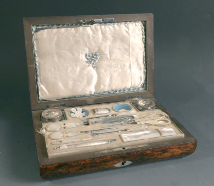Coffret à couture en ronce de bois clair à incrustations de nacre et filets cloutés; l'intéreur se compose de deux flacons carrés en cristal et d'un plateau amovible présentant douze ustensiles, la plupart en nacre gravée: dès, sceau, poinçons, porte-aiguilles, ciseaux, et