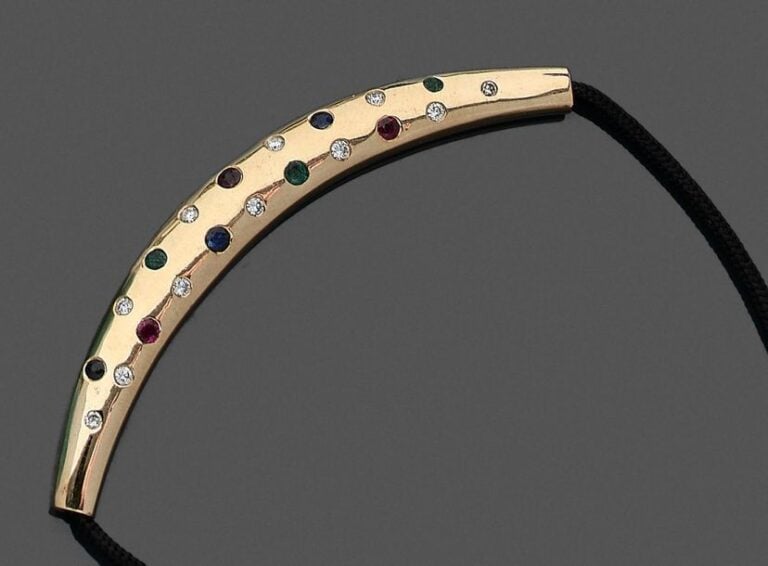 •COLLIER composé d'un élément «croissant» bombé en or jaune (750‰) parsemé de diamants, d'émeraudes, de rubis et saphirs rond