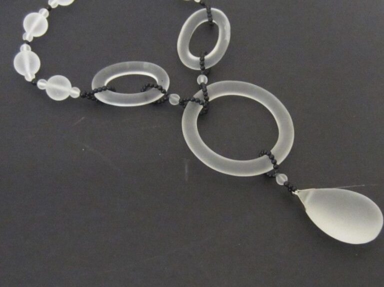 COLLIER composé d'un rang de perles de cristal de roche dépoli, alternées de petites perles d'onyx retenant un motif plus important d'anneaux ovales et circulaire terminés par une goutte piriform