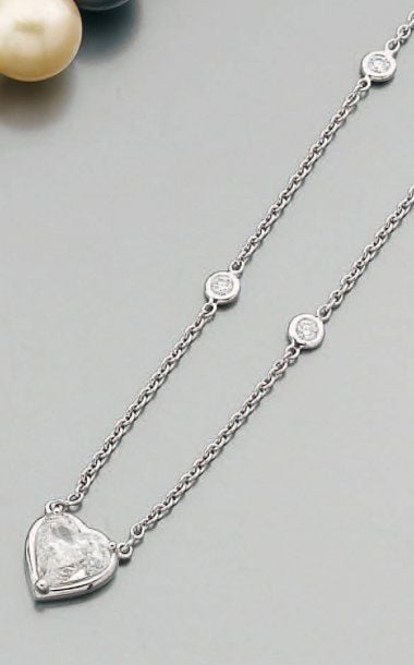 COLLIER composé d'une chaîne en or gris ponctuée de diamants taille brillant en serti clos retenant un diamant de forme coeu