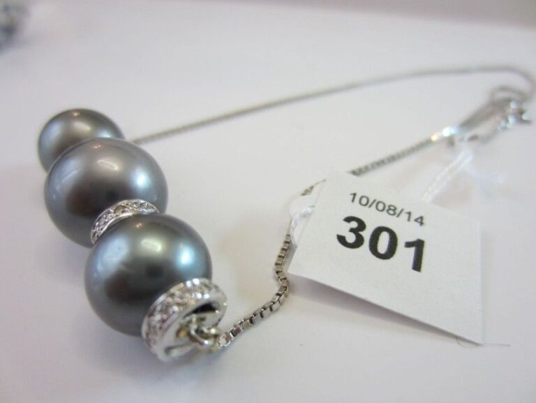 COLLIER composé d'une chaînette en or gris (750 millièmes) retenant trois perles de culture grises de Tahiti séparées par des viroles serties de diamant
