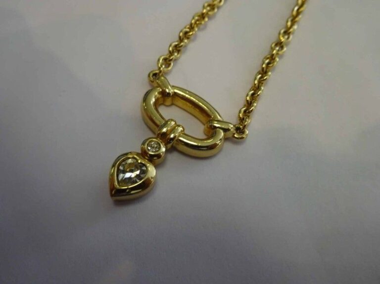 Collier en métal doré la chaîne maillée au bout un pendentif en forme de coeur fermoir aux initiales de la Maison (CD