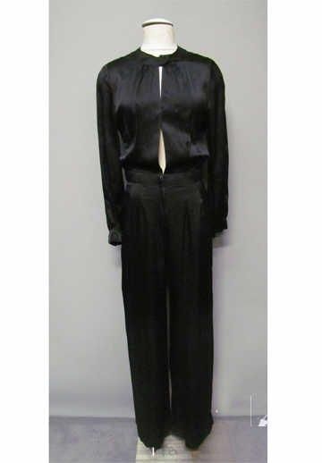 COMBINAISON-PANTALON en crêpe de soie satiné noir, encolure ronde puis échancrure jusqu'à la taille s'attachant à l'aide de pressions, celle-ci soulignée d'une ceinture à même retenant quelques pinces, rappel sur les poignets droits (env TS/M)