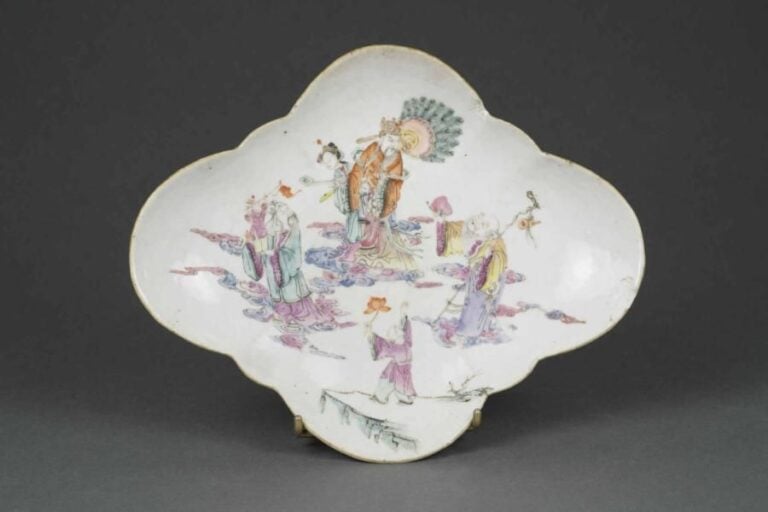 COUPE A OFFRANDES EN PORCELAINE A DECOR EMAILLE POLYCHROME DANS LE STYLE DE LA "FAMILLE ROSE" A DECOR DE LA TRIADE SANXING / FU LU SHOU, TAZZA Chine, Fin de la Dynastie Qing, Epoque fin du XIXe siècle Charmant décor des trois dieux dans le ciel parmi volutes nuageuses, des serviteurs à leurs côtés, alternance de chauves-souris et de pêches au dessous de la coupe, vagues sur le pied (éclat au côté de la lèvre floriforme
