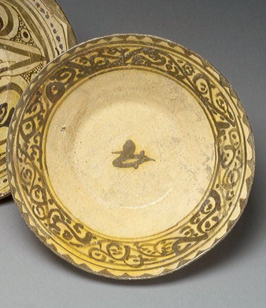 COUPE AU RINCEAU Coupe tronconique, décorée en bistre sur engobe blanc d'un oiseau au centre et d'un bandeau concentrique de motifs en rinceau bordé d'un listel de triangles en « dents de scie