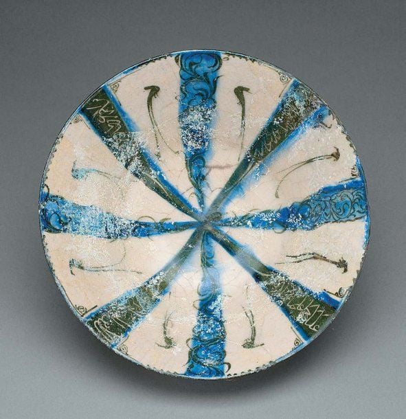 COUPE AUX BANDES RAYONNANTES ET AUX OISEAUX Coupe tronconique, décorée en bleu et noir sur fond blanc de huit bandes rayonnantes, quatre aux inscriptions cursives en réserve sur fond noir, quatre aux tiges noires sur fond bleu, délimitant huit bandes blanches ornées d'oiseau