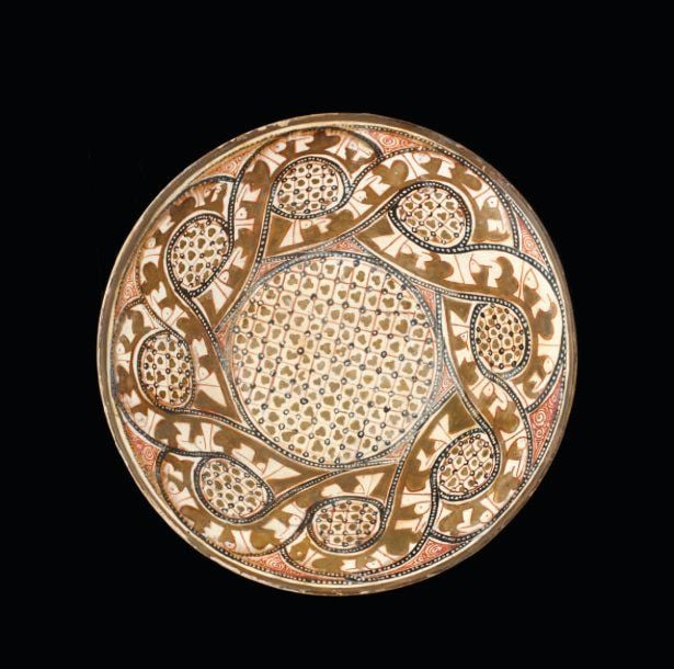 COUPE AUX ENTRELACS COUFIQUES Belle coupe tronconique, décorée en bistre, rouge et noir sur engobe blanc, sous une superbe glaçure plombeuse transparente, de bandeaux entrelacés d'inscriptions coufiques en réserves blanches, renfermant des rondeaux tapissés, comme le fond de la coupe, de croisillons aux motifs tréflé