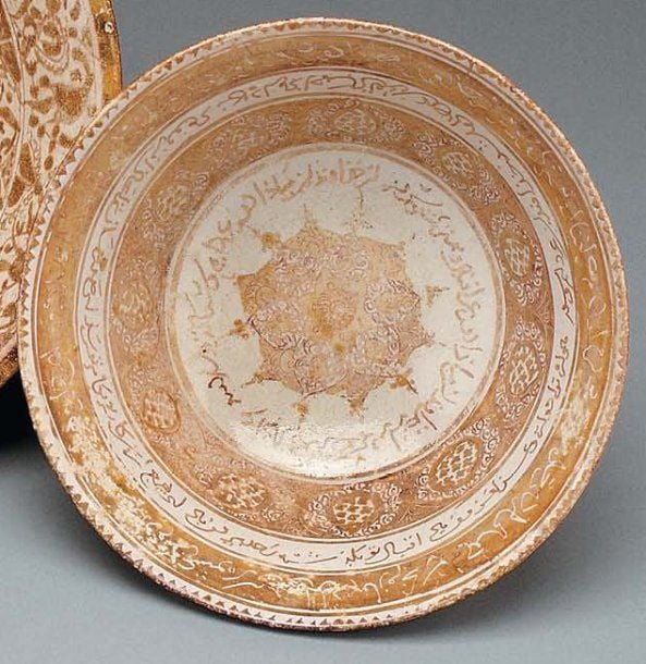 COUPE LUSTRÉE Coupe tronconique, décorée en lustre métallique brun sur glaçure opaque blanche d'un médaillon polygonal entouré de plusieurs bandeaux d'inscriptions et de palmette
