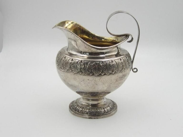 Crémier en argent sur piédouche à motif feuillagé; le corps gravé d'une importante frise de rais-de-coeurs, l'anse en volut