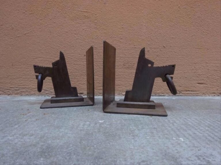 Dans le goût d'Edouard SCHENCK Charmante paire de serre-livres en fer forgé à décor de têtes de chiens stylisées, un anneau pendant dans chaque gueule, le dessus du museau crénelé et stylis