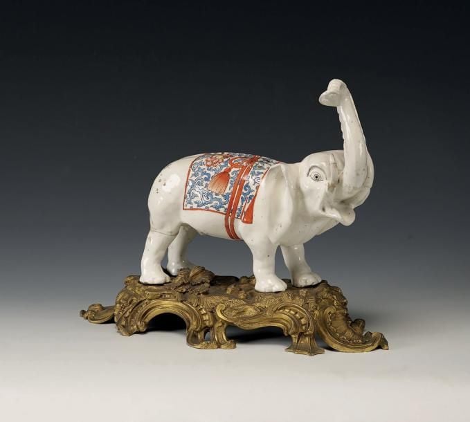 Éléphant en porcelaine blanche; il est représenté la trompe levée et le dos recouvert d'un riche étoffe nouée d'un large ruba