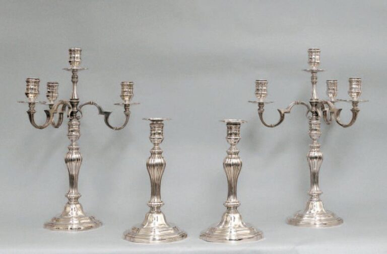 ENSEMBLE composé d'une paire de candélabres à quatre feux et une paire de flambeaux en bronze argenté, les pieds à contours et doucines, les fûts cannelé