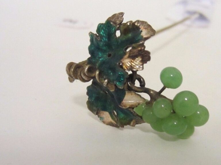 EPINGLE A CHAPEAU en métal surmonté d’un motif de « grappe » en émail (accidents et manques) et perles verte