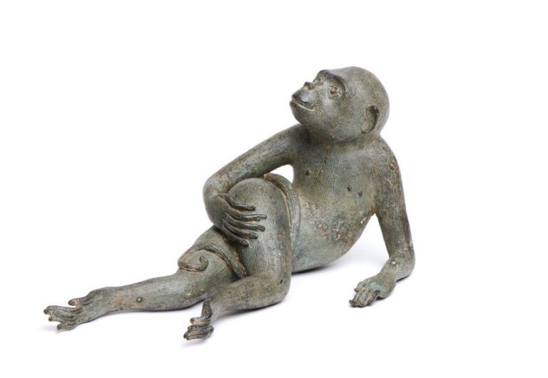 Figurine à la patine verte représentant un singe allongé (possiblement de la race des atèles) faisant une grimac