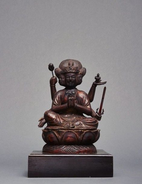 Figurine en bois laqué de couleur rouge foncé et arborant des traces de dorures figurant Batkannon, représentation de Bodhisattva Kannon avec six bras et tenant portant une pagode, un lotus et un sabre tout en faisant le geste du don (varada) et en croisant deux de ses mains devant sa poitrin