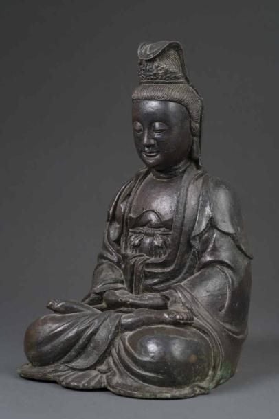 GRAND SUJET EN BRONZE A PATINE BRUNE A L'EFFIGIE DE LA DEESSE DE LA COMPASSION, GUAN YIN Chine, Fin de la Dynastie Ming, Epoque XVIIe siècle La déesse est représentée assise en padmasana, les mains jointes en dhyana-mudra, revêtant une lourde tunique, la tête surmontée d'un chignon et recouverte, pour partie, d'un pan de tiss