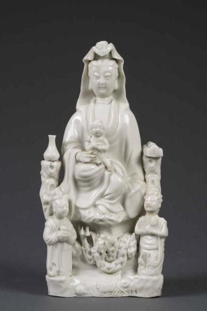 GROUPE EN PORCELAINE EMAILLEE "BLANC DE CHINE" MOULEE A L'EFFIGIE DE GUANYIN A L'ENFANT Chine, Fujian, Fours de Dehua, Dynastie Qing La déesse de la Compassion est représentée hiératique et frontale , assise en rajalalisana sur une base rocheuse, un enfant sur ses genoux, flanquée de deux vases, à ses pieds deux adorants et des dragons (cheveu, fêles de cuisson, manques dont la tête d'un serviteur