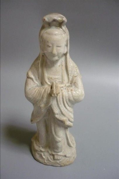 GUANYIN / DÉESSE en grès porcelaineux à glaçure craquelée céladon, représentée debout, le visage serein sommé d'un chignon que couvre un drapé, les bras en supination tenant des rouleaux sacrés (statue creuse, percement d'origine au dessous, usures