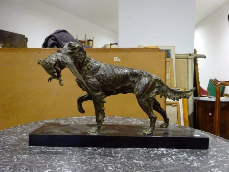 Guy DEBE (Actif XXe siècle) Setter au faisan (chien de chasse à l'arrêt, sa proie dans la gueule) Sculpture en bronze à patine verte Fixée à un socle en marbre noir Signée sur le dessus du socle Dimensions totales : H : 35 cm - L : 60 cm - l : 15 cm  A CAST-BRONZE SCULPTURE OF A HUNTING DOG BY GUY DEBE (Active 20th century)