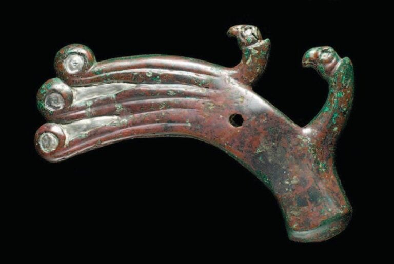 HACHE AU COUPLE D'OISEAUX Hache-marteau incurvée à douille oblongue surmontée de deux têtes d'oiseaux et dont la lame rainurée, terminée par trois volutes incrustées d'argent, évoque le plumag