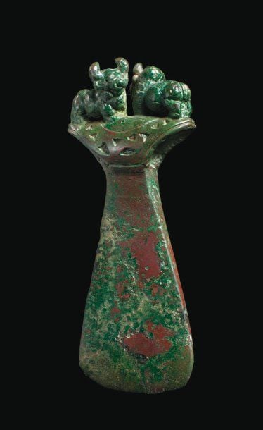 HACHE AUX ZÉBUS Lame trapézoïde, à douille ornée de cloisons triangulaires et surmontée de deux figurines de zébus debout, affrontée