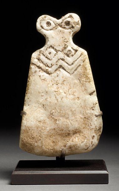IDOLE « AUX YEUX » Sculpture en albâtre, au corps trapézoïde incisé de motifs linéaires, les bras repliés sous des seins rhomboïdes aux tétons ponctués, les yeux ovoïdes à iris ponctu