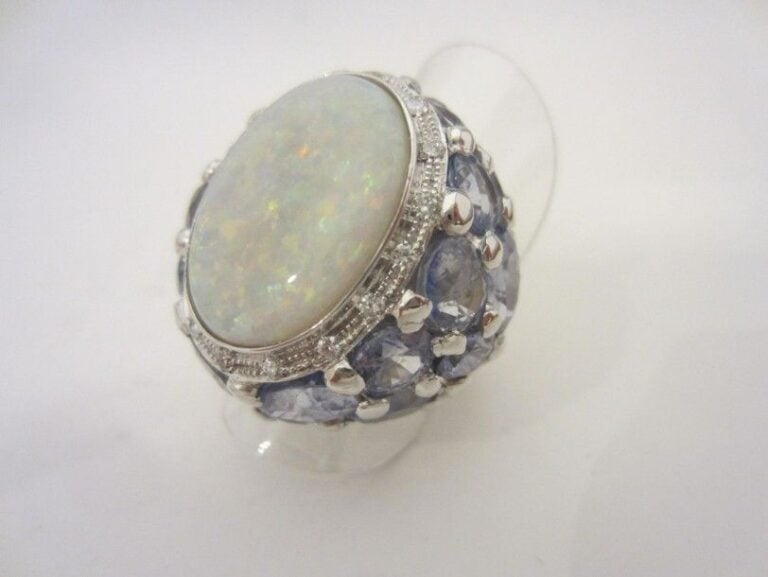 Important BAGUE en or gris 14 carats (585 millièmes) serti d’une opale de forme ovale soulignée de diamants et entouré d’un pavage de saphirs clairs