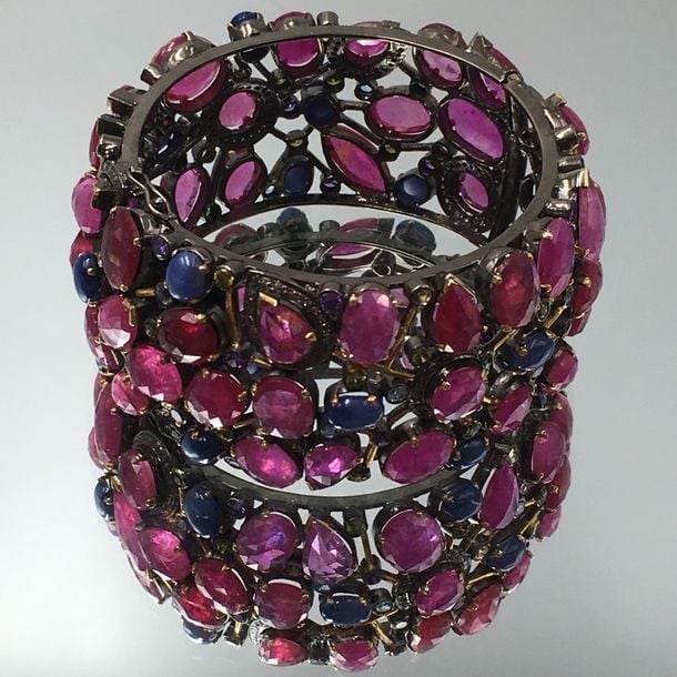 Important BRACELET MANCHETTE rigide ouvrant en argent noirci et vermeil (800 millièmes) ajouré, serti de rubis traités facettés, de pierres bleues étoilées cabochons et de pierres précieuses diverse