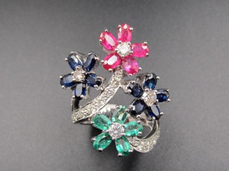 Importante BAGUE « fleurettes » en or gris (750 millièmes) ajouré serti d’émeraudes, saphirs et rubis de formes ovales et de diamants taille brillant             Doigt : 59        Poids brut : 13,6 g