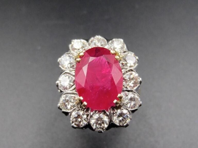 Importante BAGUE « marguerite » en or jaune et or gris (750 millièmes) serti d’un rubis de forme ovale, pesant 4,58 carats, entouré de diamants taille brillant             Le rubis est accompagné d’un rapport d’analyse gemmologique du laboratoire G       G       T       , n° 6090269, datant du 10      09      2014, attestant son poids de 4,58 carats, sa couleur Pinkish Red, chauffé        Origine : Birmanie (Myanmar)             Doigt : 55        Poids brut : 10,4 g