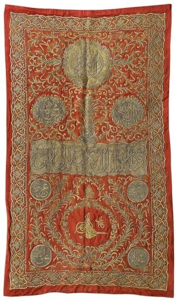 Importante tenture portant la tughra de Mahmud II Broderie de fils de métal sur velours de soie rouge Monde Ottoman, Porte la tughra de Mahmud II (Règne: 1808 -1839) Hauteur: 295; Largeur: 166 cm Dans le médaillon en partie supérieure, on peut lire l'inscription suivante: «Dieu, lumière des paradis et de la terre» (Coran 24 - al-Nur, partie du verset 25) Suivie de la shahada dans deux médaillons: «Il n'y a de Dieu que Dieu et Mahomet est son Prophète» Dans le long cartouche en-dessous, on peut lire: «Nous n'avons envoyé avant toi que des hommes à qui Nous faisions des révélation
