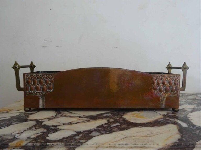 Jardinière de forme oblongue en cuivre à décor martelé façon "nid d'abeille" et à décor repousé d'arbres stylisés elle repose sur quatre pieds boules et présente deux poignées rivetées à ses extrémité