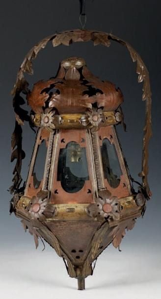 Lanterne en tôle découpée, repoussée et polychrome; de forme octogonale, elle est à décor de feuillages et fleurs stylisés et est suspendue par une anse articulée à feuillage