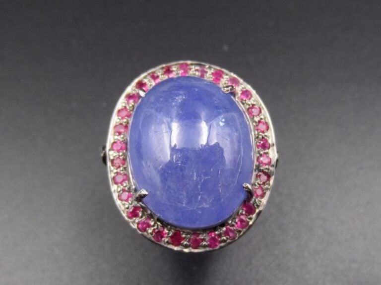 Large BAGUE ovale en argent noirci (925 millièmes) serti d’une importante tanzanite cabochon entourée de rubis Doigt : 57 Poids brut : 10,1 g