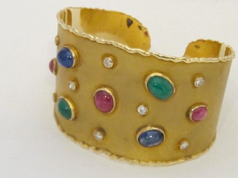 Large BRACELET manchette rigide ouvert en or jaune (750 millièmes) satiné serti d’émeraudes, saphirs et rubis cabochons de forme ovale et diamants 8 8 en serti clo