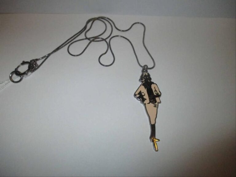Longue chaîne en métal noirci retenant un pendentif en métal noirci émaillé figurant la silhouette de Coco Chane