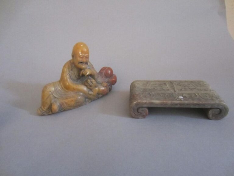 Lot comprenant deux objets en stéatite, dont un lohan endormi accompagné par un lion, et un repose-pinceaux en forme de table à rouleaux à décor de motifs archaïque